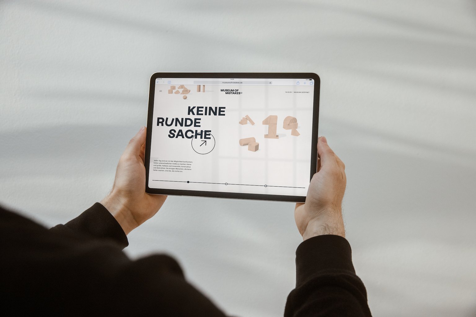 Hands holding a tablet that shows the Museum of Mistakes website with 3D wooden blocks