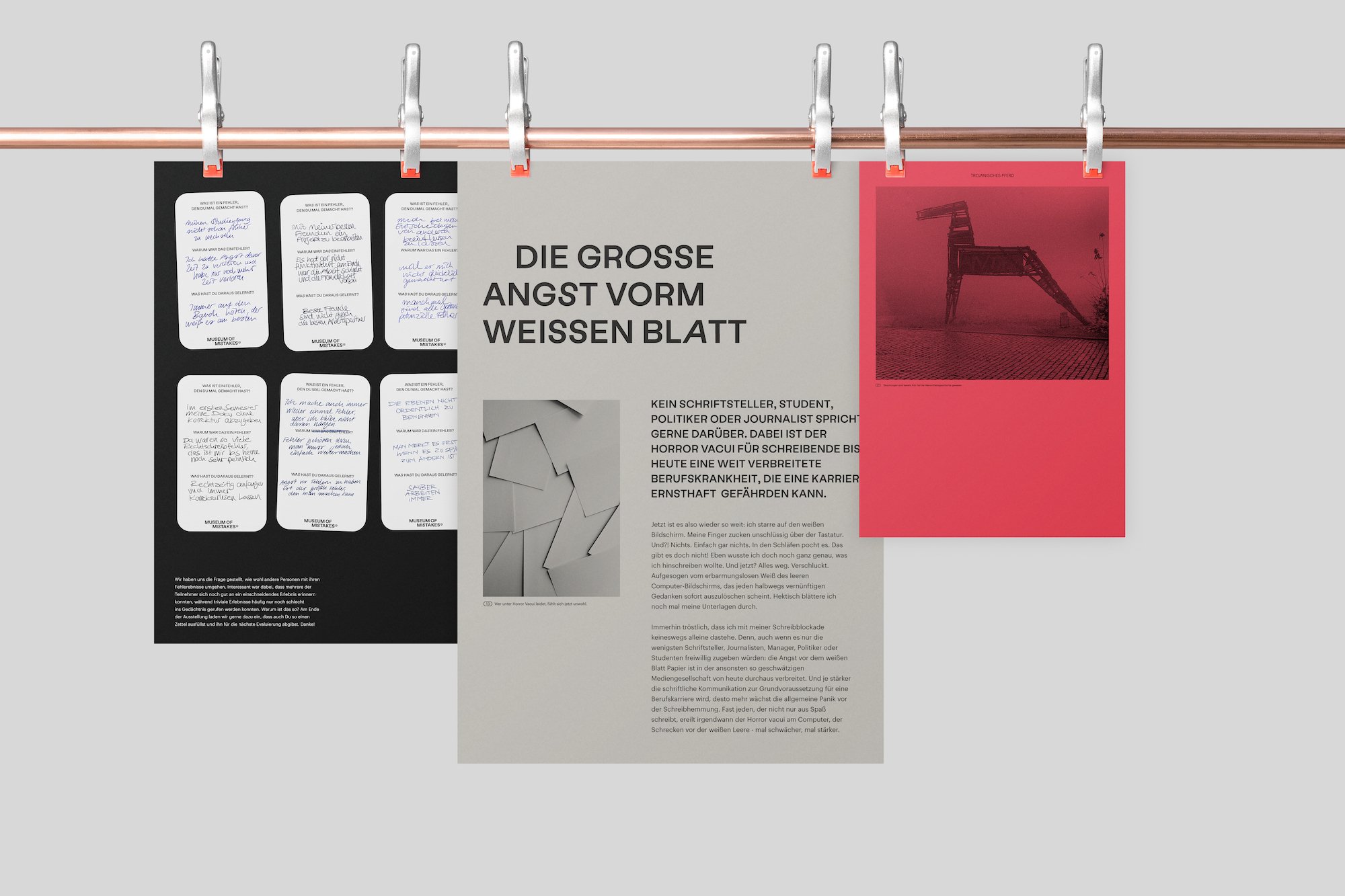 Three Museum of Mistakes posters hanging from a copper rail with clips