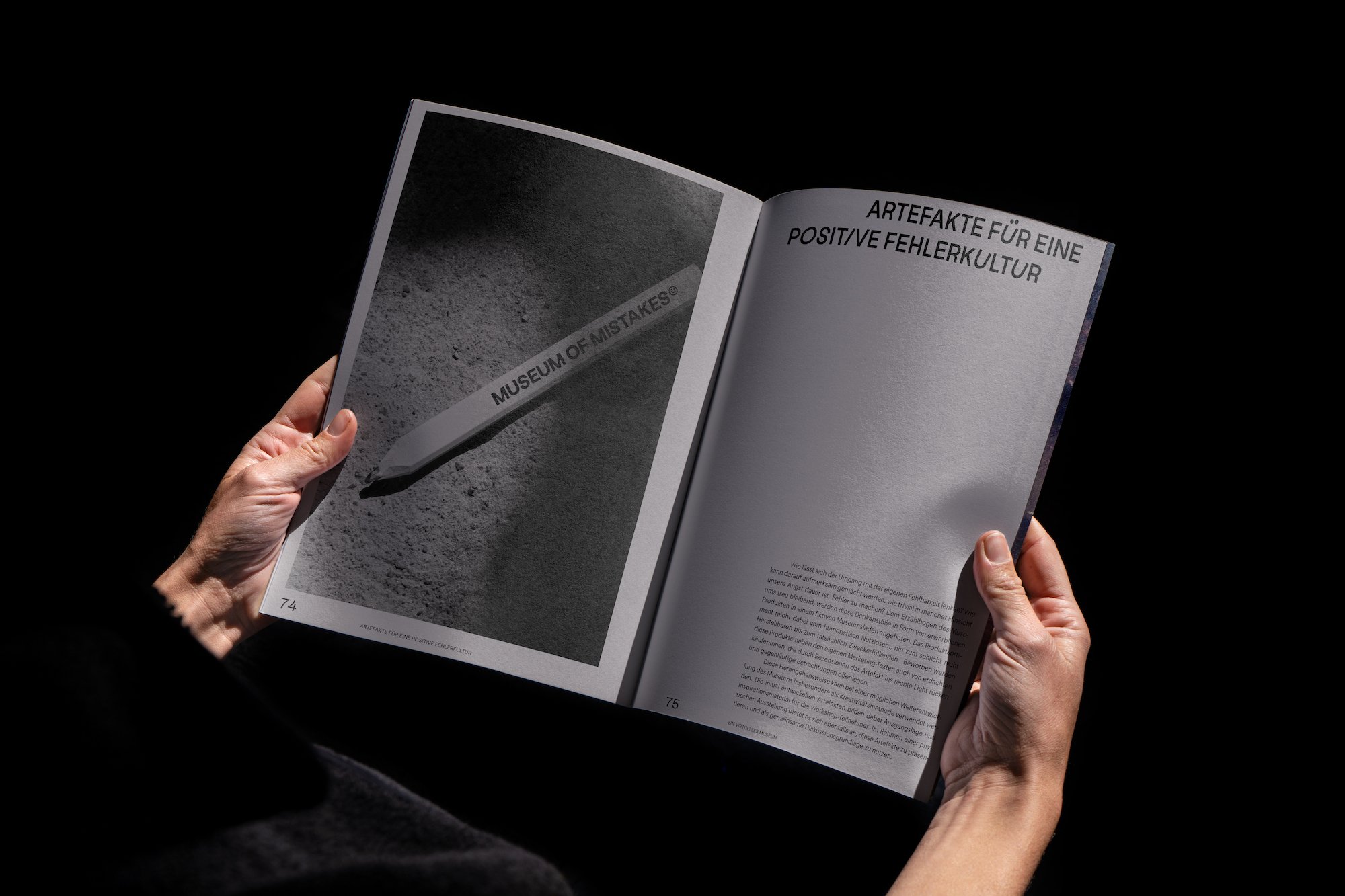Hands holding an open Museum of Mistakes publication with a photo of a branded pencil